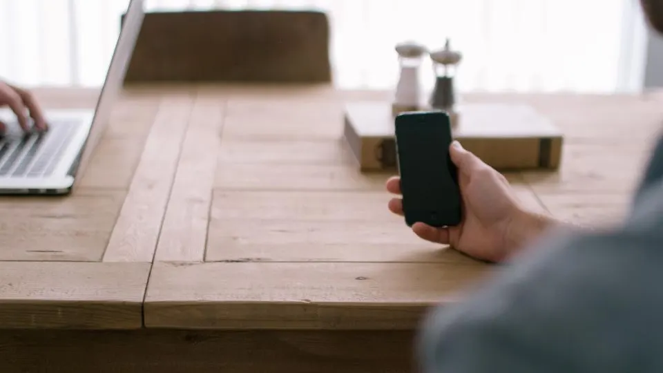 Mão segurando um iPhone sobre uma mesa de madeira